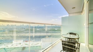 Ein Balkon mit Glastrennwand, einem Korbstuhl und einem kleinen Tisch.
