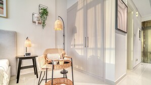 Ein modernes Zimmer mit einer Couch, einem Sessel, einem kleinen Tisch, einer Lampe und einem Kleiderschrank.