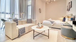 A modern hotel room with a sofa, a bed, a dining table, and a small kitchen area. - Prime Studio at Mesk 1 Midtown Dubai Production City by Deluxe Holiday Homes (Dubai)