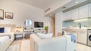 A modern hotel room with a bed, a sofa, a TV, a kitchen area, and a bathroom. - Prime Studio at Mesk 1 Midtown Dubai Production City by Deluxe Holiday Homes (Dubai)