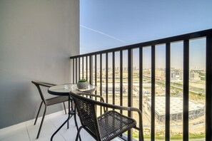 Uma varanda com uma mesa redonda e duas cadeiras de vime, com vista para uma paisagem urbana com edifícios e estradas.