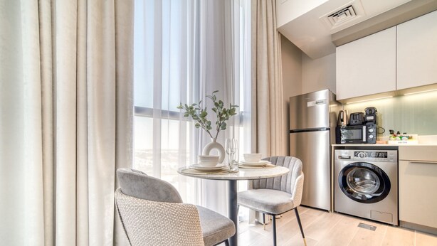A modern kitchen with a washing machine, a coffee maker, and a dining area with two chairs and a table.
