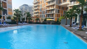 A swimming pool with lounge chairs and umbrellas, surrounded by multi-story buildings with balconies.