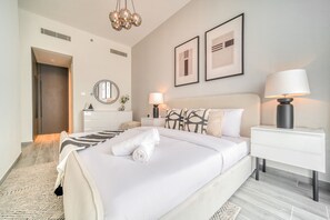 A modern hotel room with a large bed, bedside tables, a mirror, and framed artwork on the wall.
