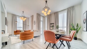 A modern living room with a dining area, featuring a sofa, armchairs, a dining table, and a chandelier.