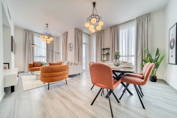 A modern living room with a dining area, featuring a sofa, armchairs, a dining table, and a chandelier.