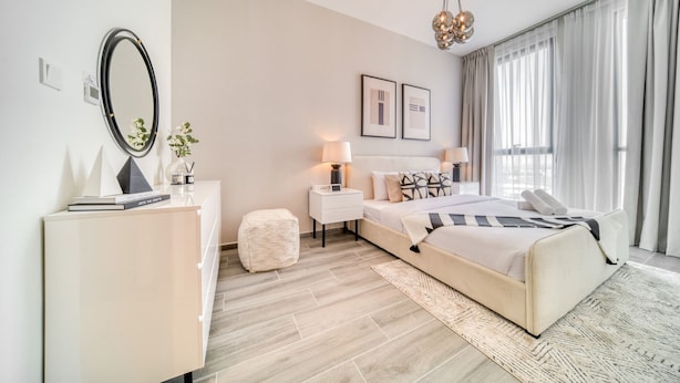 A modern bedroom with a bed, bedside tables, a mirror, and a large window with curtains.