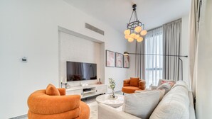 A modern living room with a sofa, armchair, and coffee table. There is a flat-screen TV mounted on the wall and a pendant light fixture above the seating area.