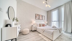 A modern bedroom with a large bed, bedside tables, a dresser, and a mirror. - Suave 2BR w/ Assistant’s Room at Mesk 1 Midtown Dubai Production City by Deluxe Holiday Homes (Dubai)
