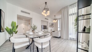 A modern dining area with a rectangular table, four chairs, and a chandelier. - Suave 2BR w/ Assistant’s Room at Mesk 1 Midtown Dubai Production City by Deluxe Holiday Homes (Dubai)