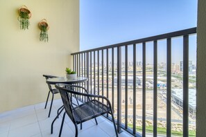 Un balcon avec une table et des chaises, deux jardinières suspendues et une vue sur la ville.