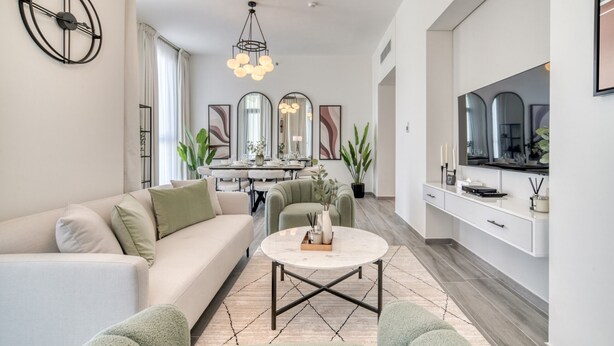 A modern living room with a sofa, coffee table, and chairs. There is a dining area with a table and chairs in the background. - Suave 2BR w/ Assistant’s Room at Mesk 1 Midtown Dubai Production City by Deluxe Holiday Homes (Dubai)