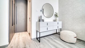 A modern bathroom with a white vanity, a round mirror, and a textured wall. - Suave 2BR w/ Assistant’s Room at Mesk 1 Midtown Dubai Production City by Deluxe Holiday Homes (Dubai)