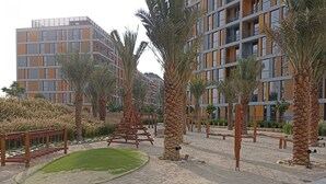 Un edificio moderno con varios balcones y un área ajardinada con palmeras y un pequeño estanque.