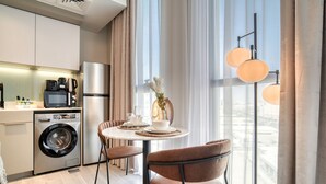 Una cocina moderna con lavadora, cafetera y refrigerador. Hay una mesa de comedor con sillas y un florero con flores.