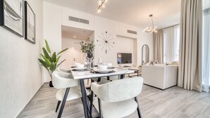 A modern dining area with a white table set for four, a potted plant, and a contemporary chandelier.