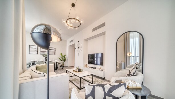 A modern living room with a sofa, coffee table, and a round chair. There is a television, a large mirror, and a floor lamp.