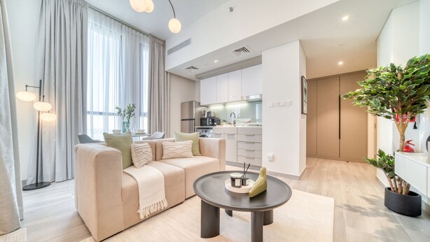 A modern living room with a sofa, a coffee table, and a kitchen in the background. - Classic Studio at Mesk 1 Midtown Dubai Production City by Deluxe Holiday Homes (Dubai)