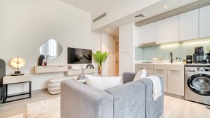 Un appartamento moderno con un divano grigio, una televisione a schermo piatto, una lavatrice e un angolo cottura.
