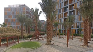 Un edificio residenziale moderno con diversi balconi e un cortile curato con palme e un'altalena di legno.