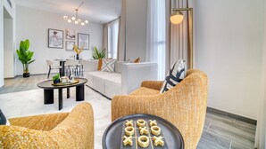 A modern living room with a sofa, armchairs, a coffee table, and a board game. There is a dining area with a table and chairs in the background.