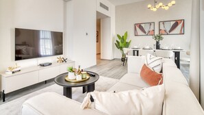 Een moderne woonkamer met een grote flatscreen televisie, een bank, een salontafel en een eethoek met een tafel en stoelen.