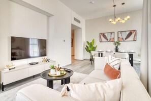 Ein modernes Wohnzimmer mit einem großen Flachbildfernseher, einer Couch, einem Couchtisch und einem Essbereich mit Tisch und Stühlen.