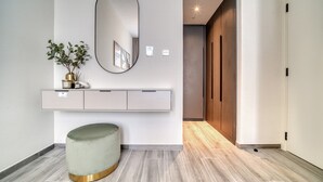 Een moderne hal met een rond poef, een spiegel aan de muur en een minimalistische console met een plant.
