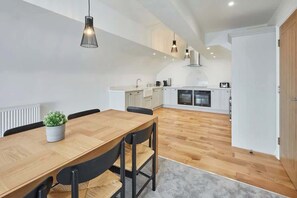 A modern kitchen with white cabinets, a wooden dining table, and pendant lighting.