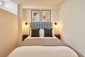 A bedroom with a bed, two wall-mounted light fixtures, and two framed artworks above the bed.