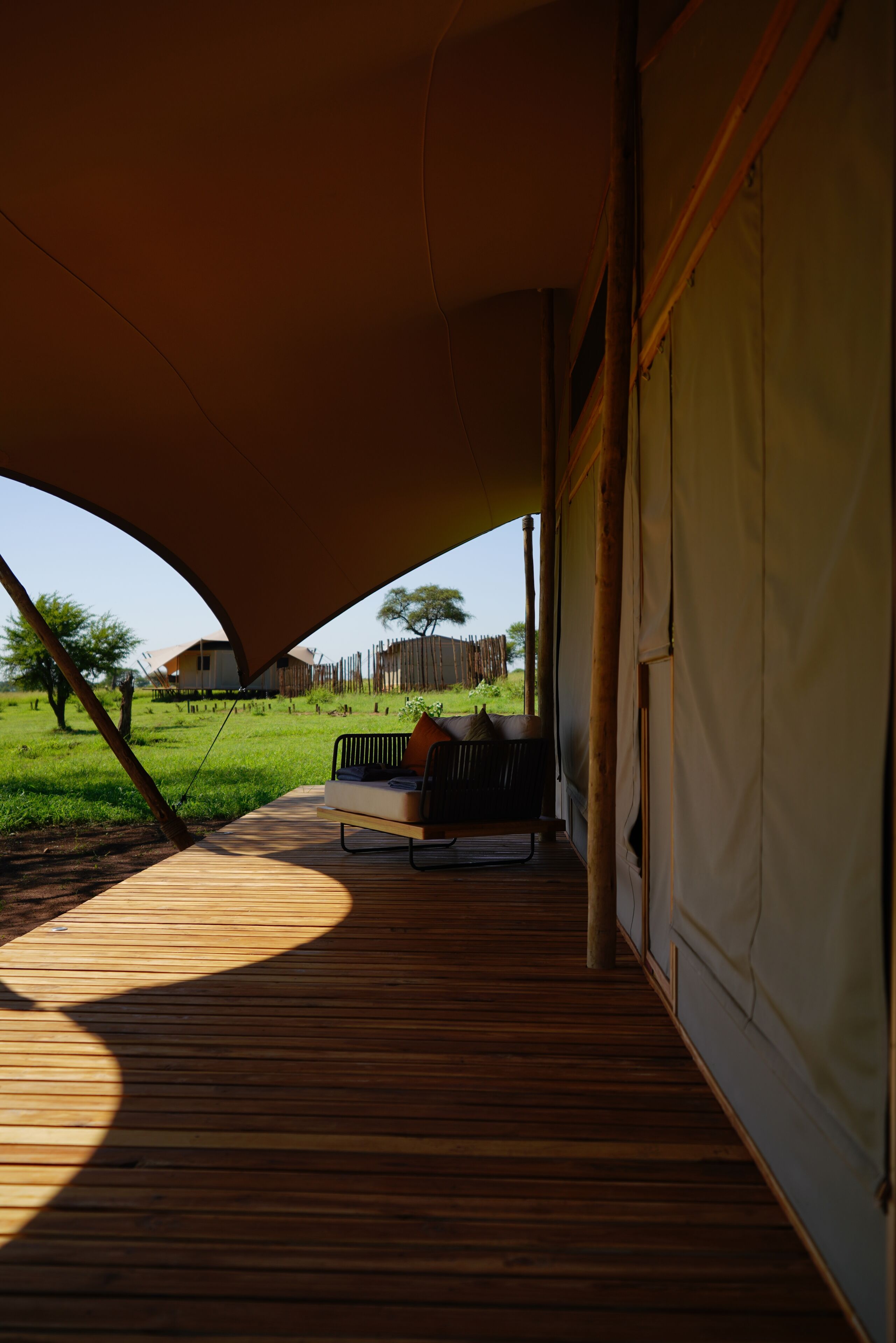 A wooden deck with a covered seating area, a view of a grassy field, and a building in the background.