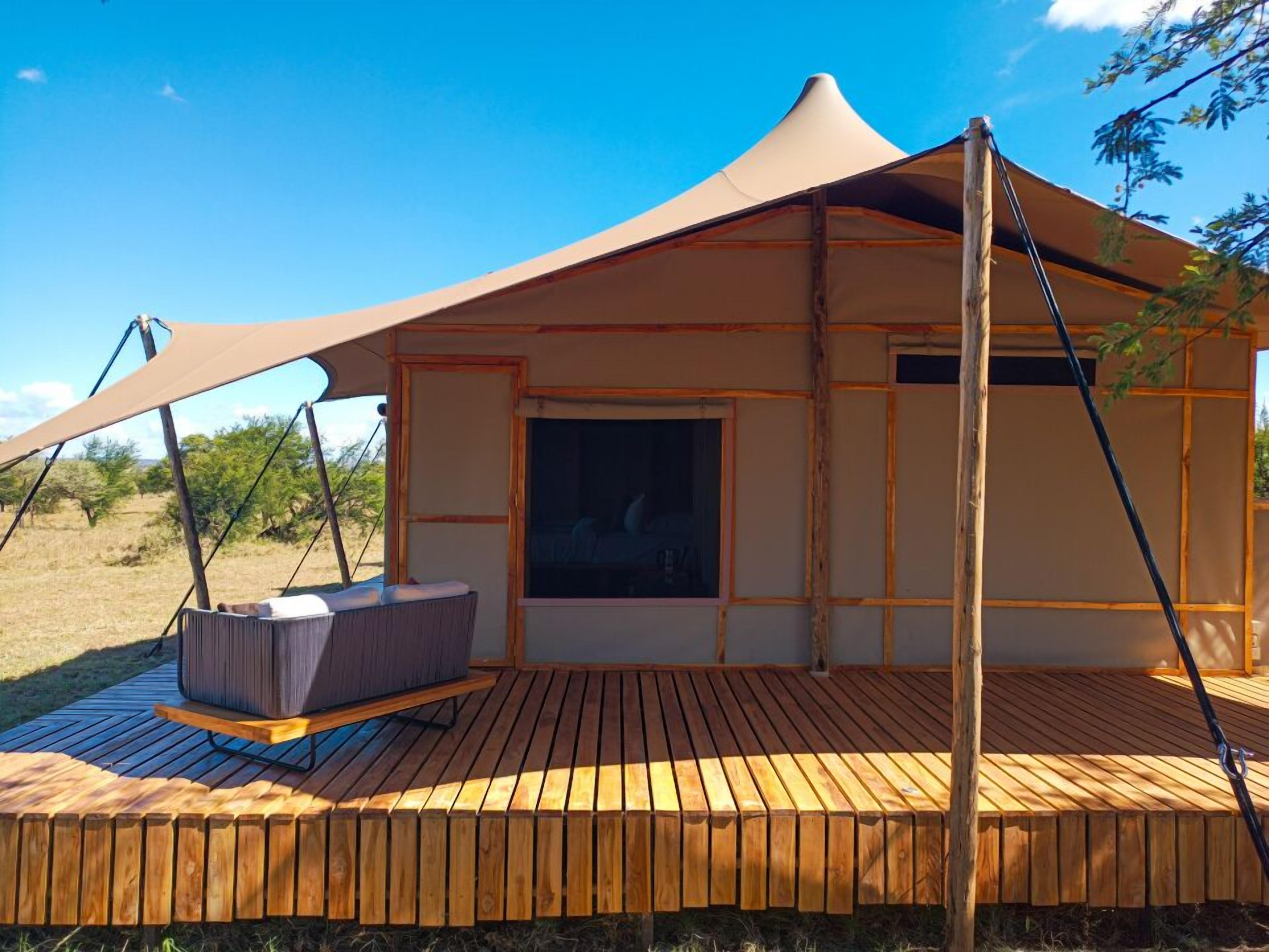 A tent with a wooden deck, a cushioned seating area, and a window.