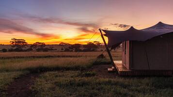 Alojamento em tenda com vista para um pôr do sol sobre um campo gramado.