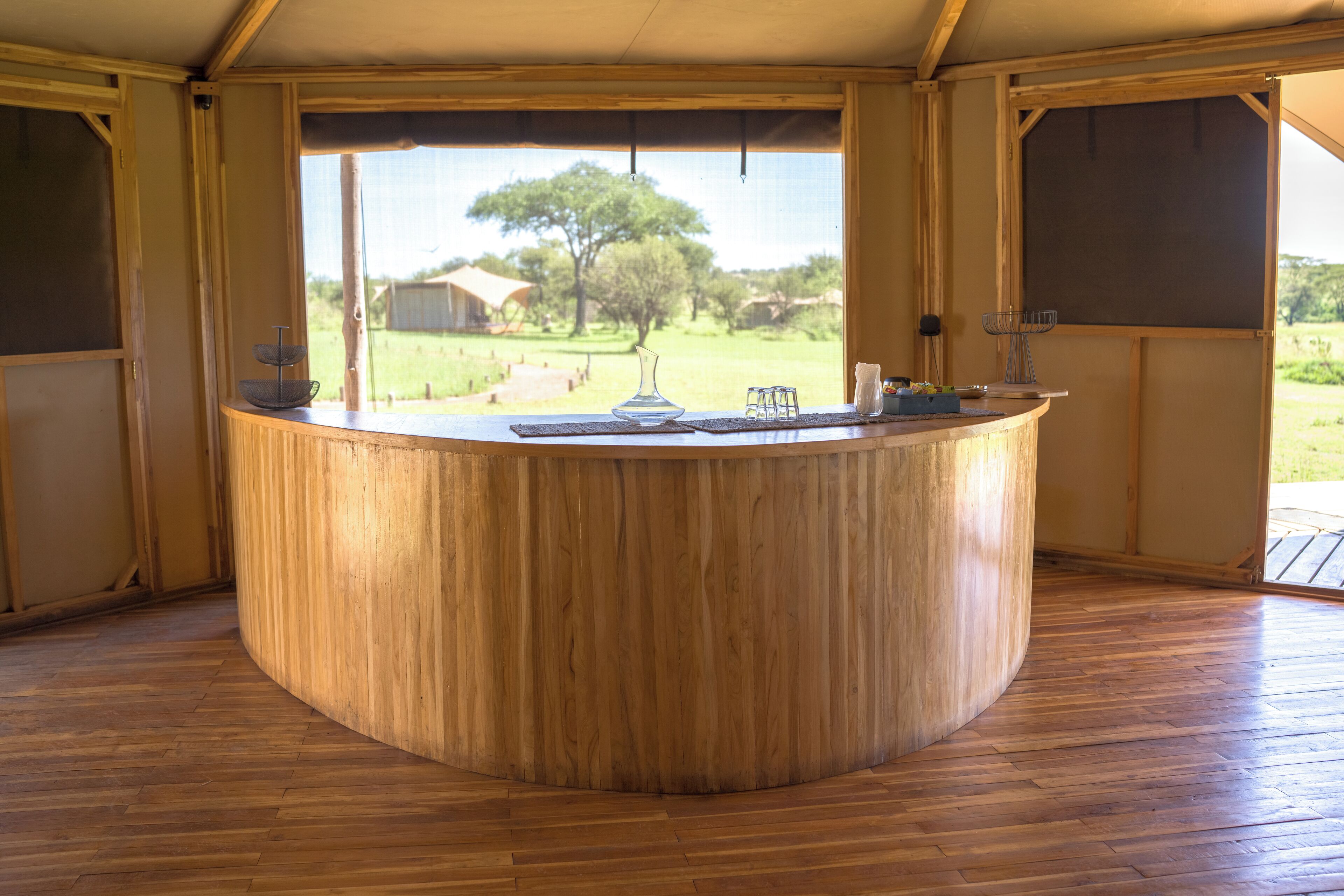 Zona de bar con barra de madera y vista a un campo cubierto de césped y árboles.