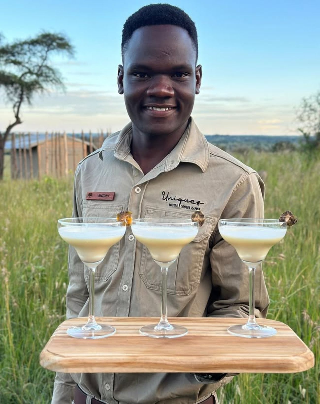 A person holding a wooden tray with three martini glasses.