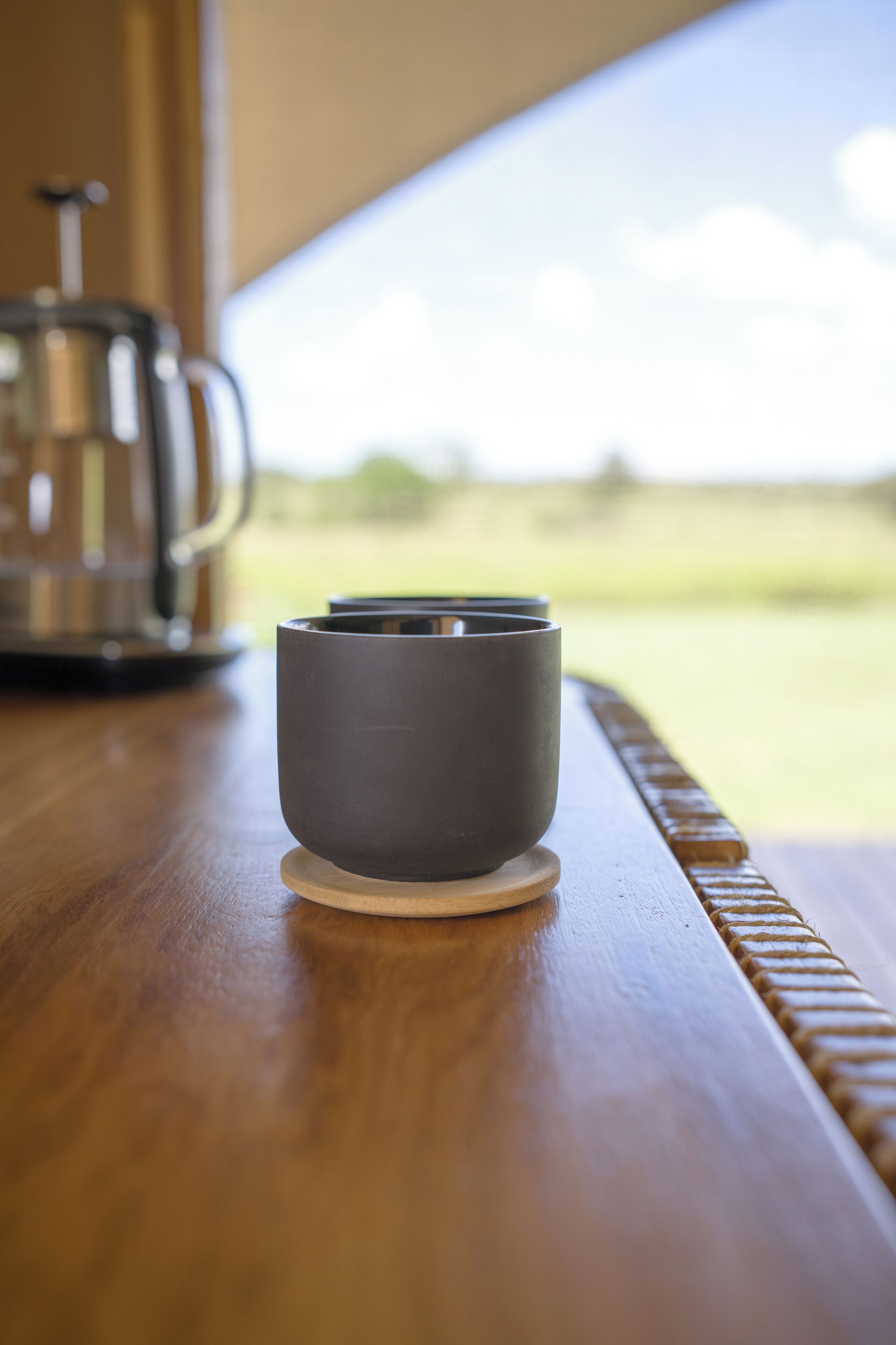 Una mesa de madera con una taza oscura y una cafetera de acero inoxidable.