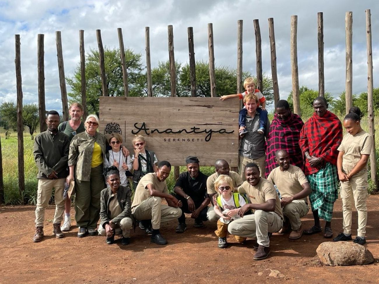 Un groupe de personnes posant devant une enseigne en bois sur laquelle est inscrit le nom « Anantya Serengeti ».