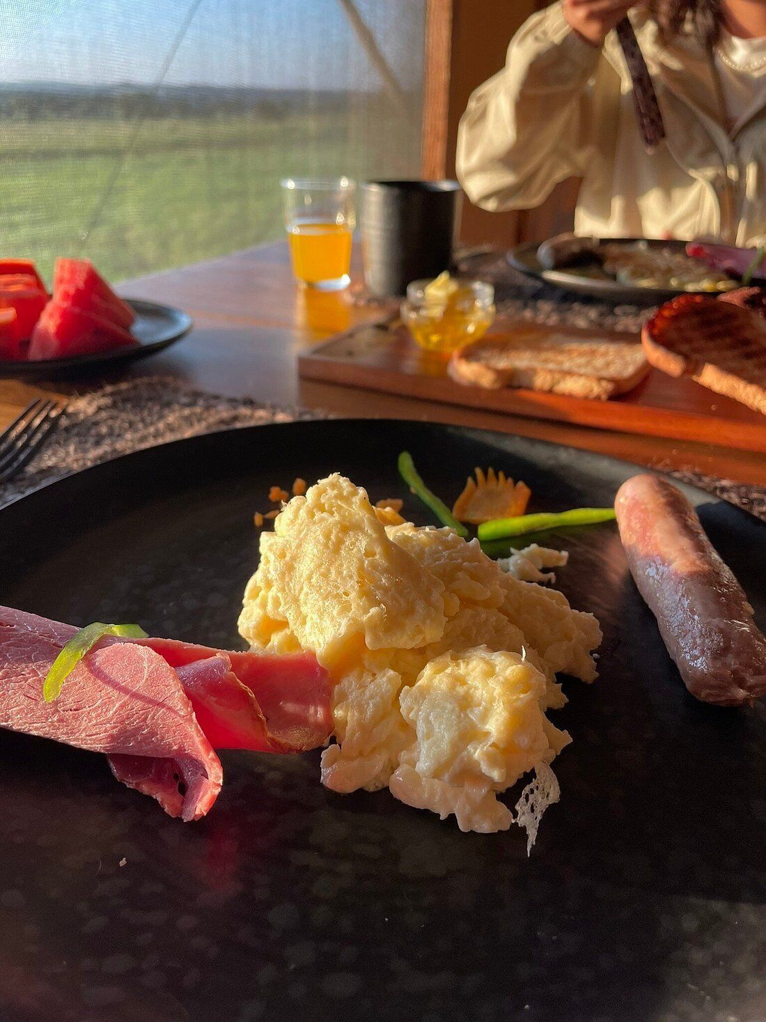 A breakfast plate with scrambled eggs, ham, and sausage.