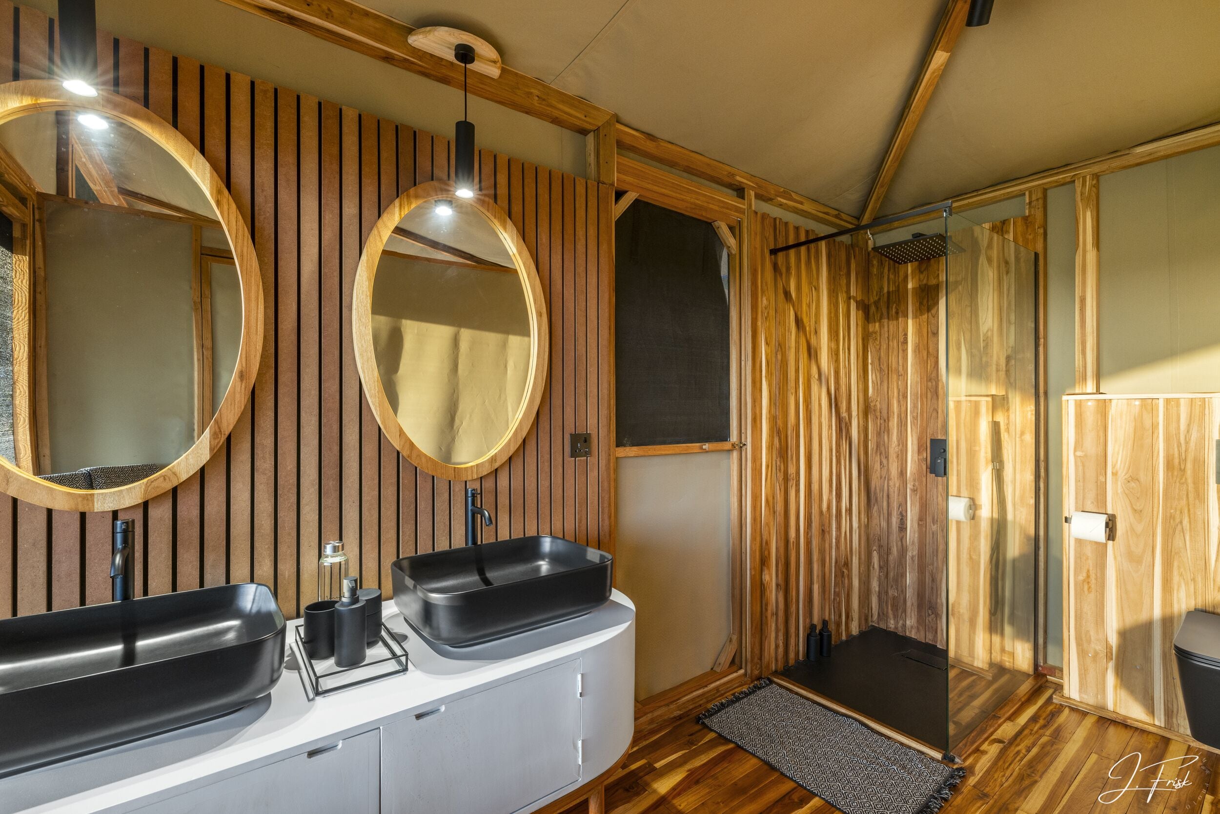 A modern bathroom with wooden paneling, a double sink, and a glass shower enclosure.