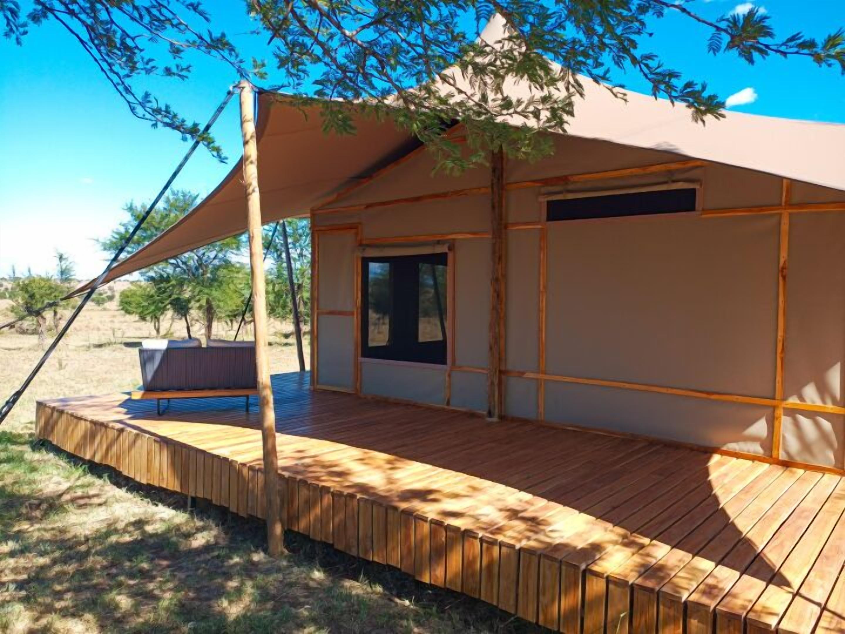 Una terraza de madera con un área de estar cubierta y un ventanal con vistas a un paisaje natural.