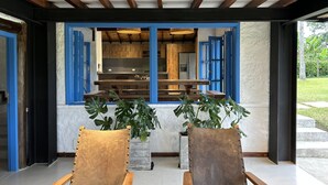 Zona esterna con sedute in legno e piante in vaso, che conduce a una cucina con mobili azzurri e design moderno.