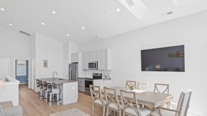 A modern kitchen with white cabinets, a dining area with a wooden table and chairs, and a large window.