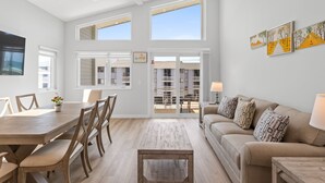 A spacious living area with a wooden dining table, comfortable seating, a sofa with patterned cushions, and artwork on the walls.