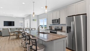 A modern kitchen with a large island, stainless steel appliances, and a dining area with a view. - Seadragon 2 | Pet-Friendly w/ Rooftop Deck + Ocean Views! (Carolina Beach)