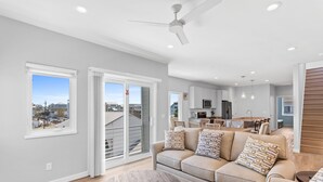 A modern living room with a sofa, a coffee table, and a view through a sliding glass door to the outside. - Seadragon 2 | Pet-Friendly w/ Rooftop Deck + Ocean Views! (Carolina Beach)