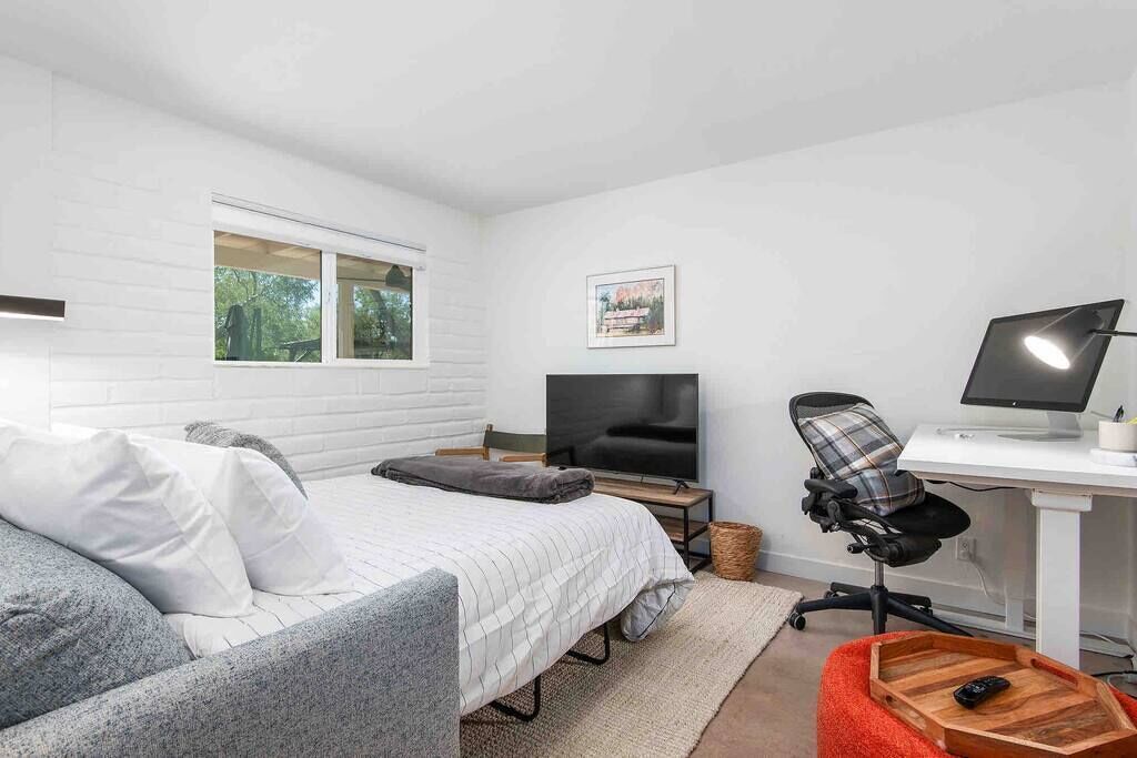 Une chambre à coucher avec un lit, un bureau avec un ordinateur, une chaise et un téléviseur.