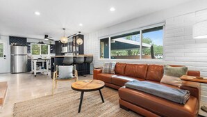 A modern living space with a leather sofa, a round coffee table, and a kitchen area with stainless steel appliances. - Foothills Summer Escape | Private Pool & Mtn Views (Tucson)