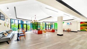 Eine geräumige Lobby mit hoher Decke, großen Fenstern und verschiedenen Sitzbereichen, darunter Sofas und Tische.