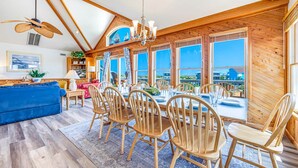 A spacious dining area with wooden chairs and a table, large windows with a view, and a ceiling fan. - Semi-Oceanfront Dog Friendly w/ Pool, Hot Tub, Cargo Lift, Nearby Beach Access (Salvo)