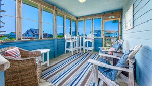 A sunlit porch with wicker chairs, a striped rug, and a view of houses through large windows. - Semi-Oceanfront Dog Friendly w/ Pool, Hot Tub, Cargo Lift, Nearby Beach Access (Salvo)